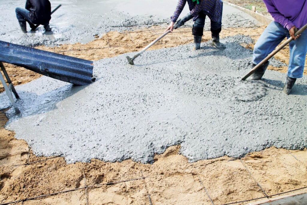 Workers spreading wet concrete over a prepared base with rakes