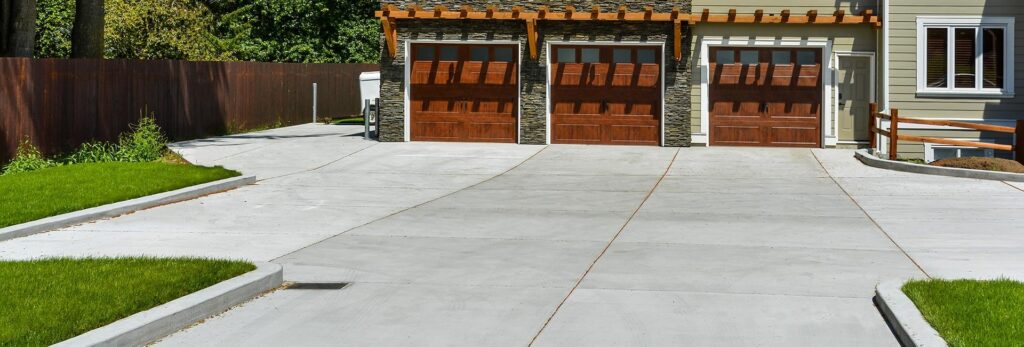 Broad concrete driveway in front of a three-car garage with wooden doors
