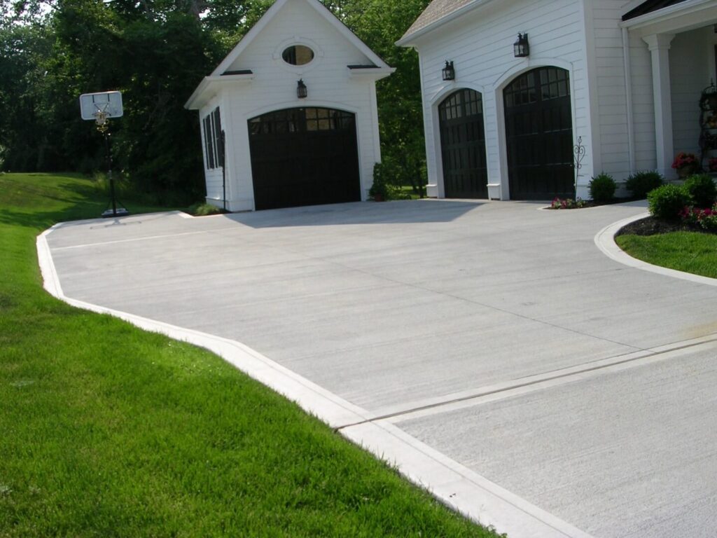 White house with a long curved concrete driveway and a basketball hoop by the garage